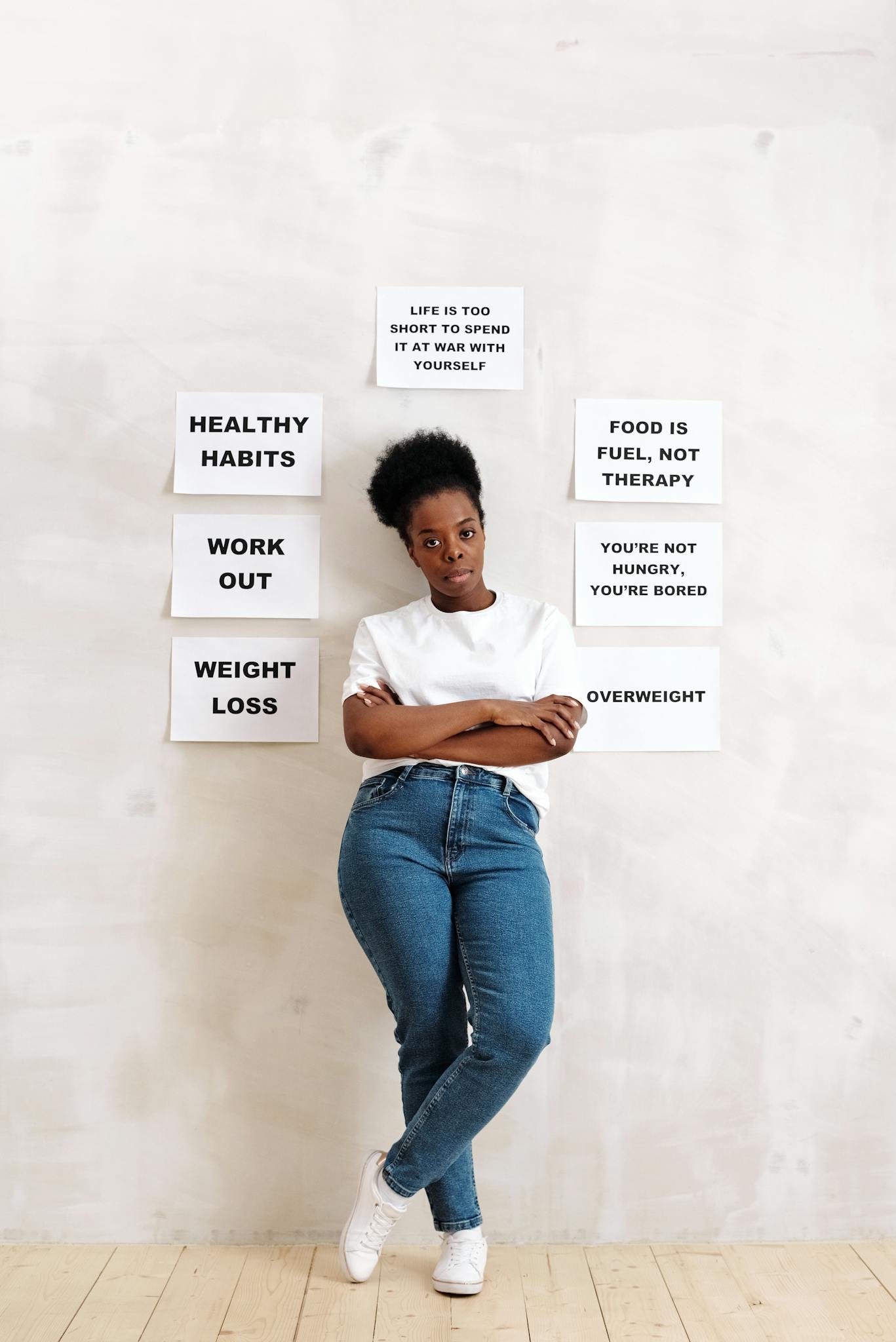 A woman standing against a wall with signs promoting healthy lifestyle habits and messages.