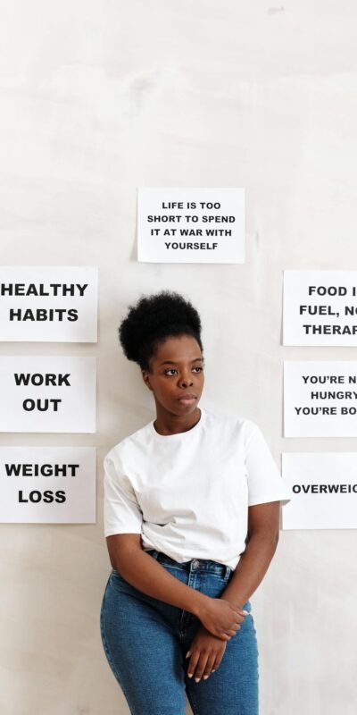A woman stands by motivational self-care and wellness quotes on a wall.